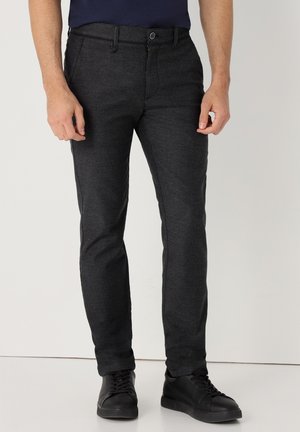 Pantalones tejidos de color gris oscuro con un corte ajustado, que cuentan con un cierre de botón y cremallera, bolsillos frontales y una textura suave. Combinados con zapatillas negras.