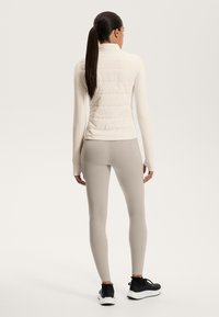 Lightweight, cream puffer jacket with a high collar, paired with light beige leggings and black athletic shoes, featuring a smooth texture.
