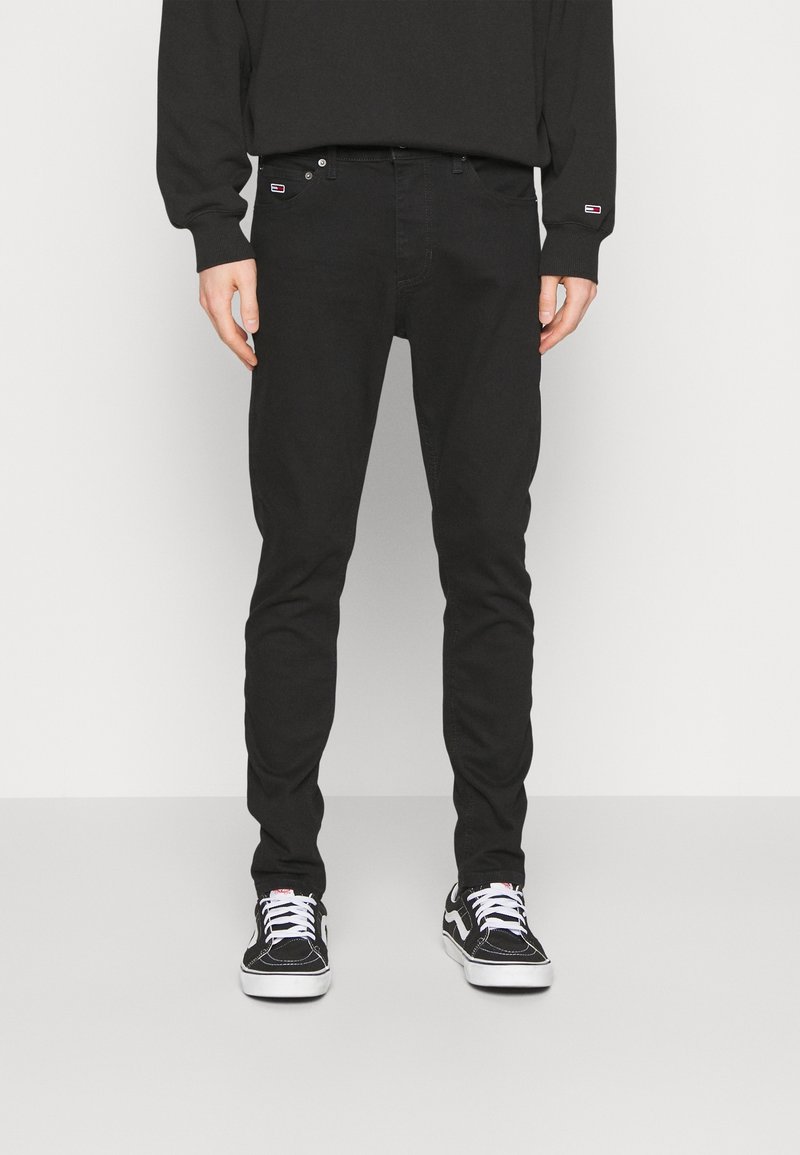 Svarta denimjeans med smal passform, fem fickor och subtil branding. Bärs med svarta sneakers med vita snören och gummisålar.