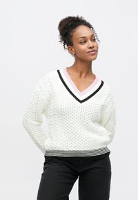 Hvid kabelstrikket sweater med V-hals, med lyserøde og sorte stribede detaljer på kraven og en sort ribbet kant.