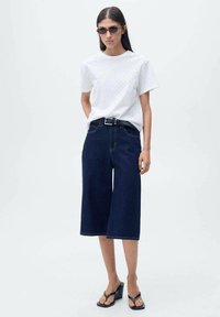 Hvid kortærmet skjorte med øjelets tekstur, parret med mørkeblå vide denim culotter og sorte platform sandaler.