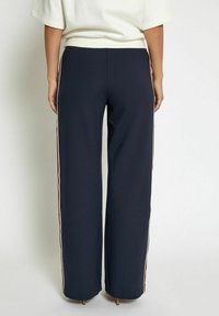 Navy wide-leg pants with contrasting side stripes in white and red, made from smooth fabric, featuring an elastic waistband.