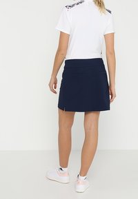 Navy skirt with a smooth fabric, featuring two back pockets and a slight side slit. Paired with a white top and white sneakers with pink accents.