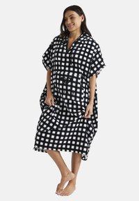 Black and white checkered oversized hooded poncho with short sleeves, featuring a front pocket and drawstring neckline, made from soft fabric.