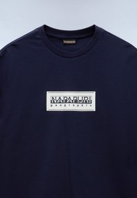 Navy blue cotton t-shirt with a crew neck, featuring a white rectangle graphic that includes "NAPAPURI" and "geographic" text.