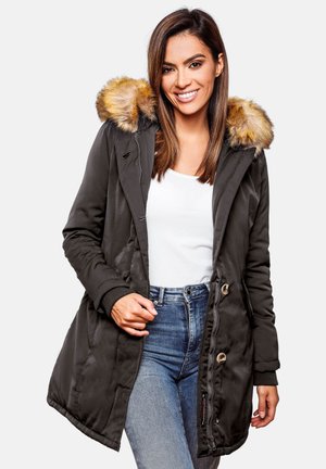 Parka vert foncé avec une capuche en fausse fourrure, fermeture éclair et boutons, poches latérales et poignets côtelés, portée sur un haut blanc et un jean bleu.