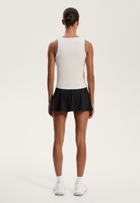 Vit linne med svarta accenter, tillsammans med en svart veckad kjol. Outfiten har en figurnära design och en mjuk textur.