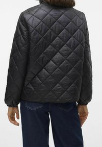 Černá prošívaná bunda s stojáčkem, hladkým materiálem a elastickými manžetami, v kombinaci s modrými širokými džíny.