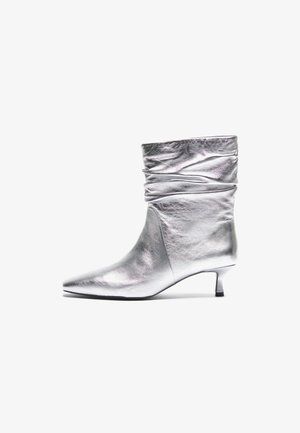 Zilveren metallic enkellaars met een slouchy bovenkant, puntige neus, kitten heel en een gladde textuur. Heeft een glanzende afwerking en een minimalistisch ontwerp.