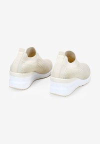 Baskets en tricot beige avec un dessus texturé, un col élastique et une semelle légère blanche. Présente un design montante pour un enfilage facile.