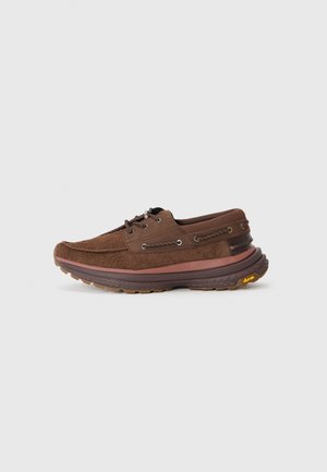 Brune semska sko med rund tå, snörning, vibram-sula och multi-texturerade accenter längs sidan.