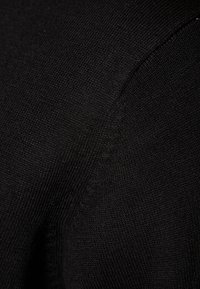 Svart stickat tyg med en fin textur och subtila variationer som framhäver ett jämnt och slätt vävmönster över ytan.