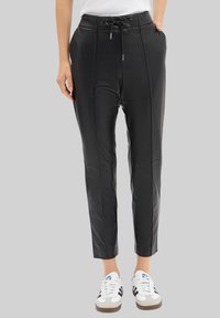 Pantalons en simili cuir noir avec plis à l'avant, taille élastique et cordon de serrage. Coupe fuselée à la cheville, associés à des baskets blanches.