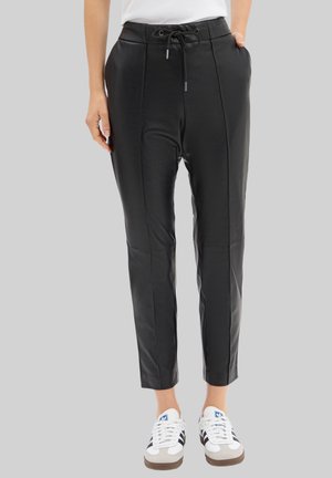 Pantalons en simili cuir noir avec plis à l'avant, taille élastique et cordon de serrage. Coupe fuselée à la cheville, associés à des baskets blanches.