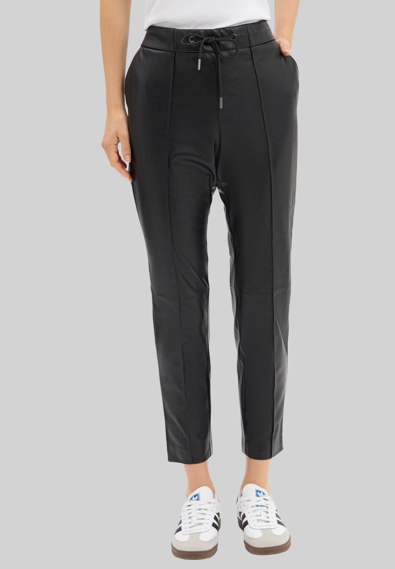 Pantalons en simili cuir noir avec plis à l'avant, taille élastique et cordon de serrage. Coupe fuselée à la cheville, associés à des baskets blanches.