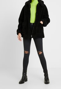 Czarna kurtka z sztucznego futra z kołnierzem, z dwoma przednimi kieszeniami. Noszona na jasną zieloną bluzkę z golfem, w połączeniu z ciemnymi podartymi dżinsami i czarnymi botkami.