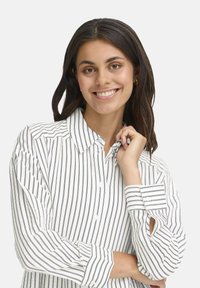 Long-sleeve blouse featuring white fabric with vertical navy stripes, button closure, and a collar. Includes roll-tab sleeves and a relaxed fit.