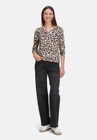 Langärmeliges Oberteil mit Leopardenmuster und V-Ausschnitt, kombiniert mit hochgeschnittenen dunklen Jeans und weißen Sneakers, präsentiert ein lässiges Outfit.
