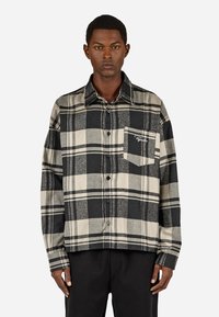 Fekete és bézs kockás ing, gombos kialakítással, hosszú ujjakkal, elülső zseb brokáddal, puha anyagból készült.