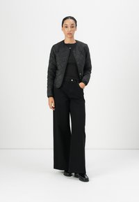 Black quilted jacket with a round neckline, paired with a fitted black top and high-waisted black wide-leg trousers. Black shoes complete the outfit.