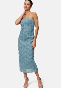 Robe midi sans bretelles, moulante, en tissu texturé bleu clair avec un motif floral. Accessoirisée avec des talons argentés à lanières.