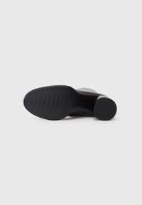 Botte en cuir noir avec une semelle texturée. Elle présente une finition lisse, un bout arrondi et un talon bas. La semelle extérieure est dotée de bandes horizontales pour une meilleure adhérence.