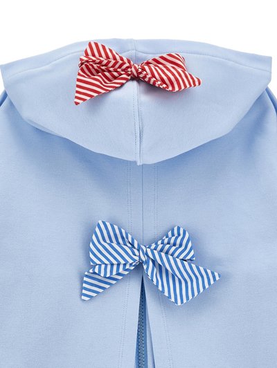 Svetlo modra oblačila z zadrgo in dvema pritrjenima pentljama, eno rdeče-bele črtasto na kapuci, eno modro-bele črtasto pod zadrgo.