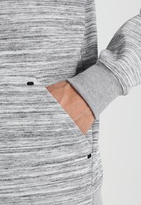 Sudadera a rayas gris y blanca con un bolsillo tipo canguro, puños de canalé y una tela texturizada con un acabado suave.