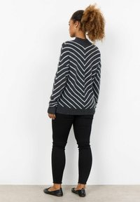Un pull gris foncé avec des rayures en chevron blanches, des manches côtelées et un ourlet côtelé. Associé à un jean skinny noir et des ballerines noires.