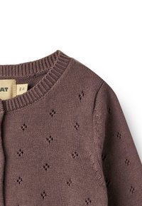 Brun strikket babycardigan med små diamantformede hulmønstre og ribstrikket rund halsudskæring, størrelseslabel synlig indeni kraven.