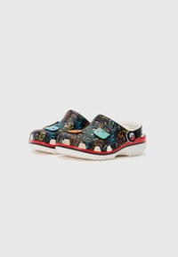 Clogs made of black rubber with multicolored cartoon patterns, white textured soles, and red accents on the side and bottom edges.