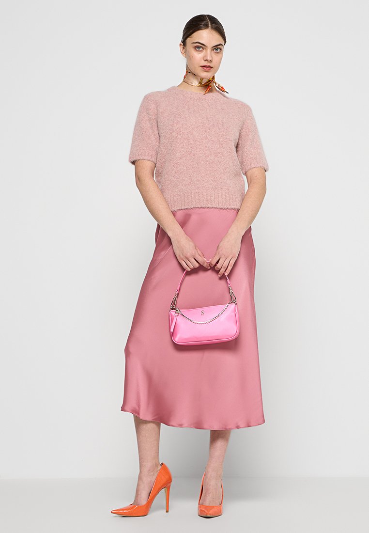 Maglione corto a maniche corte in maglia pelosa di un rosa chiaro, gonna midi in satin rosa, tacchi alti arancioni e una piccola borsa lucida rosa con tracolla a catena.