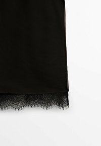 Abito nero con materiale trasparente e orlo in pizzo nero intrecciato, caratterizzato da motivi delicati e un taglio dritto. Design minimalista.