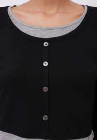 Black cropped top made of soft fabric with a rounded neckline, featuring six metallic buttons down the front and a gray inner layer.
