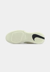 Světlá podešev tenisek z texturované gumy, s černým designem loga Nike a vlnovým vzorem pro lepší přilnavost.
