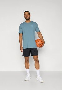 Meeste vabaaja outfit, mis koosneb sinisest lühikese varrukaga T-särgist ja mustadest lühikestest pükstest, hoides oranži korvpalli ning kandes valgeid tossusid ja sokke.