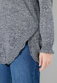 Jersey gris y blanco con un dobladillo en forma de scallop y tela texturizada. Combinado con jeans de mezclilla azules, que muestran un ajuste relajado.