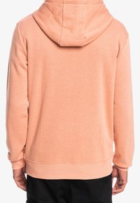 Persikka huppari, jossa on kiristysnauha huppuun, ribbatut hihansuut ja helma. Pehmeä kangas ja yksinkertainen muotoilu ilman näkyviä kuvioita tai grafiikoita.