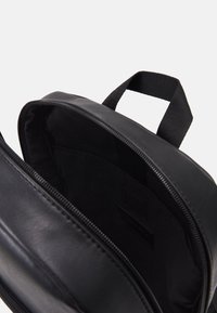 Sac à dos en cuir noir avec une fermeture éclair ouverte. Il présente une texture lisse, un design simple et un intérieur en tissu avec une petite poche.