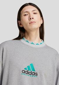 Grauer Pullover mit türkisfarbenen Akzenten, einem runden Halsausschnitt mit Streifenmuster und einem gestickten schwarzen und türkisfarbenen "adidas Equipment"-Logo.