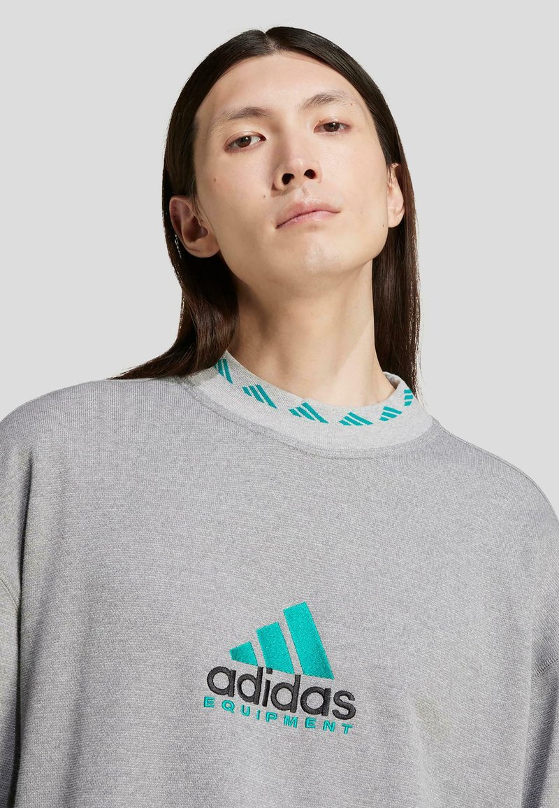 Grå sweatshirt med turkosa accenter, rund hals med ett randigt mönster och en broderad svart och turkos "adidas Equipment"-logotyp.