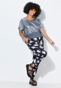 Metallisch graues Kurzarmoberteil, gemusterte schwarze Hose mit weißen Wolkenformen und schwarze Sandalen mit Riemchen und dicker Sohle.