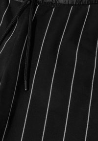 Czarna tkanina z wąskimi, białymi pionowymi paskami, z detalem sznurka w talii. Tekstura wydaje się miękka i lekko fakturowana.