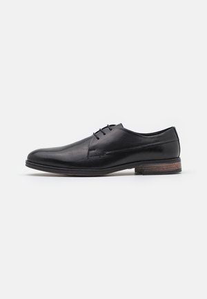 Scarpa da uomo in pelle nera con finitura liscia, design con lacci, punta arrotondata e un accentuato tallone marrone testurizzato.