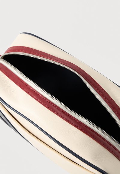 Pochette rectangulaire beige avec une fermeture éclair argentée partiellement ouverte et une bordure rouge autour de l'ouverture sur un fond uni.