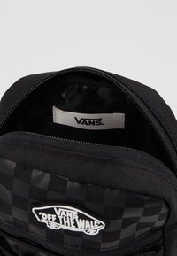 Schwarzer Rucksack mit einem karierten Muster, ausgestattet mit einem Reißverschluss-Hauptfach und einem "VANS Off The Wall"-Logo-Patch auf der Vorderseite.