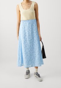 Virkat toppi vaaleassa sävyssä, yhdistettynä siniseen brodeerattuun hameeseen, jossa on kukkakuvioita. Yhdistetty harmaisiin lenkkareihin ja mustaan käsilaukkuun.