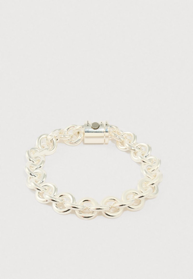 Sudraba ķēdes rokassprādze ar savienotām apaļām un ovāla formas saitēm, plakanu virsmu un cilindrisku aizdari. Gluda, spīdīga apdare.