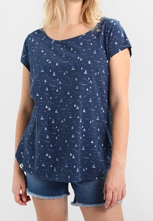 Femme portant une chemise bleu marine à manches courtes avec de petits motifs de voiliers et un short en jean avec des ourlets effilochés.