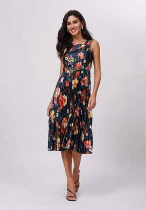 Robe plissée florale avec une base bleu foncé, ornée de fleurs vibrantes rouges, jaunes et blanches. Design asymétrique, tissu léger, longueur genou.